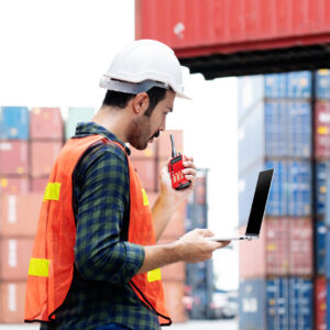 Container workers use laptops to work in port warehouses. Wear a hardhat to be safe at work.